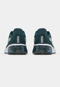 Ζευγάρι σκουροπράσινα παπούτσια Puma, εμφανιζόμενα από την πίσω πλευρά, με λευκές σόλες και μπλε ενδιάμεσες σόλες με σχέδιο, σε απλό φόντο.