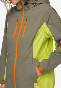 Chaqueta resistente al agua con un cuerpo gris y lados de un verde brillante. Presenta cremalleras y detalles en naranja, capucha ajustable y bolsillos laterales.