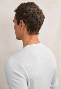 Jasnoszara koszula z długim rękawem wykonana z miękkiego, gładkiego materiału. Posiada okrągły dekolt oraz widoczne przeszycia wzdłuż szwów na ramionach.