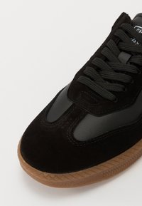 Schwarzer Sneaker aus einer Kombination von Wildleder und glattem Leder, mit strukturierten Schnürsenkeln und einer Gummi-Sohle in Lederoptik mit Diamantmuster.
