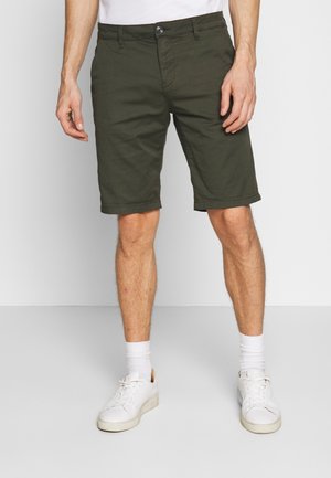 Olivengrønne bomuldsshorts med en lige pasform, forlommer og knaplukning. Kombineret med hvide sneakers og op-rullede buksekanter.