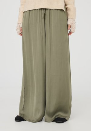 Pantaloni a gamba larga di un verde oliva chiaro, realizzati in un tessuto morbido con una vita regolabile, abbinati a un maglione a maglia crema e scarpe nere.