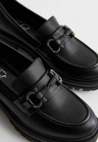 Mocasines de cuero negro con un acento decorativo de cadena, textura suave, suela de perfil bajo y diseño de punta redonda.