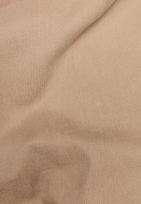 Tissu beige avec une surface lisse et texturée présentant un motif en côtes diagonales, plissé à plusieurs endroits. Matériau doux et flexible.