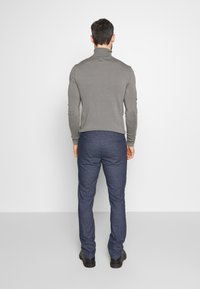 Grå turtlenecktröja med långa ärmar i kombination med mörkblå strukturerade byxor. Svarta skor fulländar outfiten. Bakvy mot en enfärgad bakgrund.