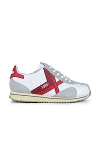 Zapatilla blanca con acentos de ante gris y detalles de cuero rojo. Presenta una cruz roja prominente y una suela de goma texturizada. Amarrada con cordones blancos.