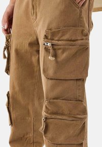 Pantalones cargo marrones con múltiples bolsillos con cremallera, una textura de tela duradera y un diseño de corte holgado, ideales para un uso práctico.
