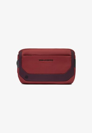 Bolso de hombro de tela roja con una textura suave, que presenta un acento en púrpura oscuro, cierre de cremallera y un logo grabado en la parte frontal.