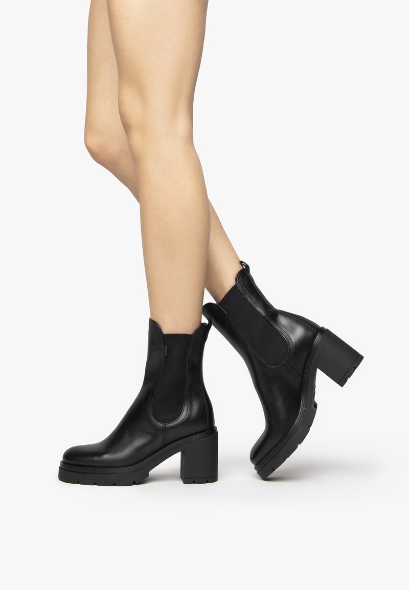 Bottines en cuir noir avec un talon épais, des panneaux latéraux élastiques et une finition lisse. Semelle texturée pour une meilleure adhérence et stabilité.