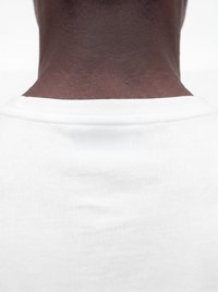 Rückenansicht einer Person mit dunkler Haut, die ein weißes T-Shirt mit Rundhalsausschnitt vor schlichtem weißem Hintergrund trägt.