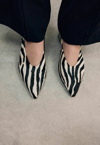 Zebra-patterned pointed-toe shoes made of soft, textured material in black and cream, showcasing an open cut design.