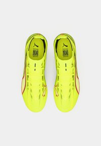 Gule løbesko med et slankt design, der har en tekstureret overdel, kontrasterende rødt accent og et logo på siden.