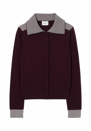 Mujer con un cárdigan morado abotonado con cuello a rayas, falda midi beige con abertura, sandalias doradas y lleva un bolso blanco al hombro.