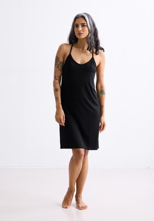 Zwarte mouwloze jurk van gladde stof met een ronde halslijn en een rechte pasvorm die tot halverwege de dij valt.