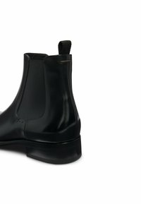 Chelsea boot in pelle nera con finitura liscia, pannelli laterali elastici e un'etichetta per indossarla facilmente. Punta rotonda e tacco basso.