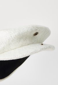 Gorra blanca de fieltro con forma redondeada, que presenta un interior negro, hardware en tono dorado y una superficie texturizada.