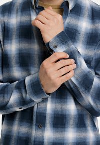 Camicia a quadri blu navy e azzurro chiaro in morbido tessuto, con colletto button-down e polsini a un bottone. Texture con una finitura spazzolata.