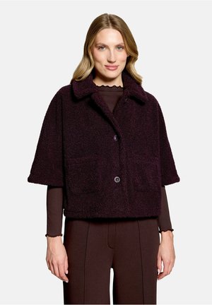 Femme portant une courte veste texturée violet foncé avec un grand col, une fermeture à boutons, et des manches longues et un pantalon marron foncé assortis.