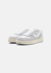 Zapatillas de cuero con un diseño en blanco y gris claro, que cuentan con una puntera texturizada, cordones planos y una suela de goma crema, con pequeñas perforaciones.