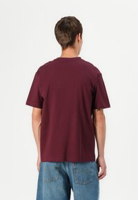 Burgunderfarbener Baumwoll-T-Shirt mit Rundhalsausschnitt und kurzen Ärmeln, getragen mit hellblauen Jeans aus Denim mit Gesäßtaschen.