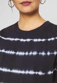 Black t-shirt with a round neckline, featuring horizontal tie-dye stripes in white. The fabric appears soft and lightweight.
