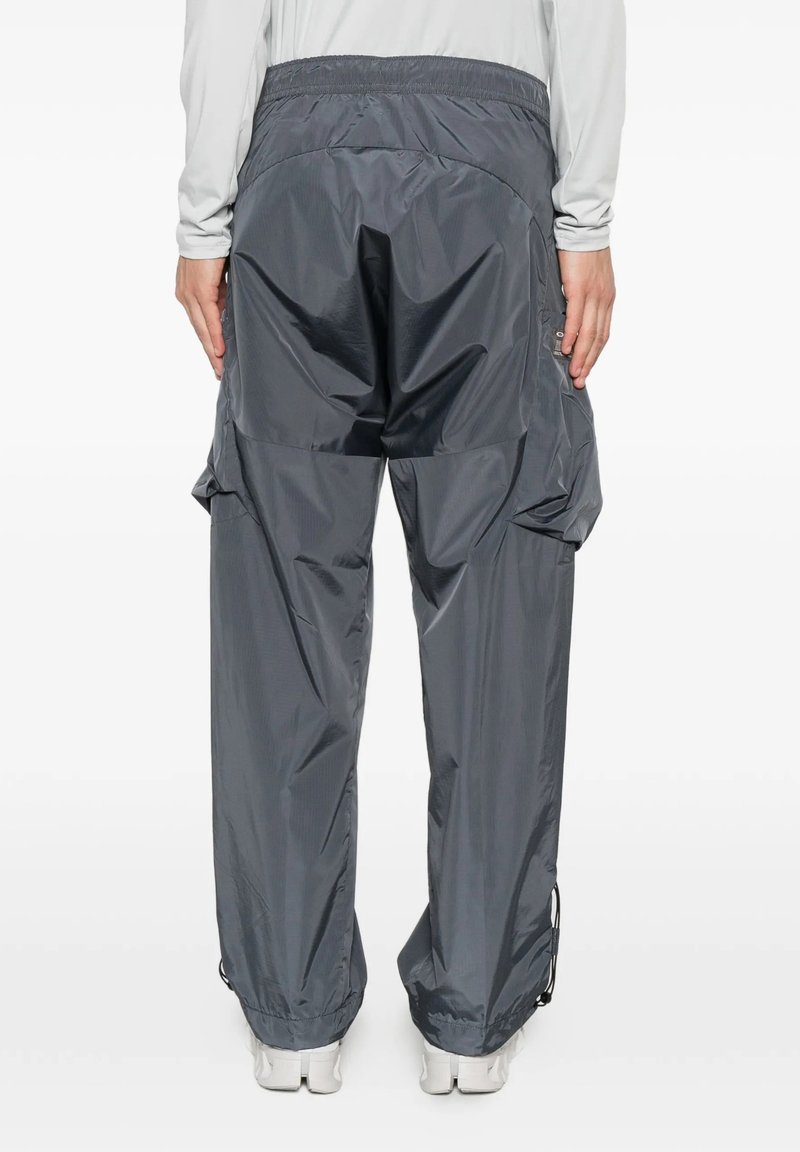 Persona che indossa pantaloni cargo di nylon grigio scuro larghi con polsini elastici e molte tasche, vista da dietro.