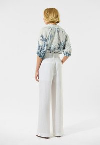 Lichte, gebloemde blouse met blauwe palmontwerpen; witte, wijde linnen broeken met een gladde textuur en subtiele naden.