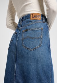 Denim skirt with a high waist, blue color, and a tan leather label at the back. Features distinctive stitching and two back pockets.