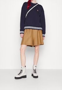 Granatowa bluza z białymi paskami na dole i mankietach, brązowe szorty oraz białe wysokie buty z czarną podeszwą i sznurowadłami.