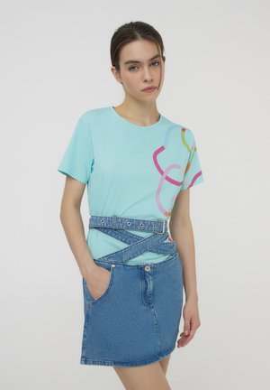T-shirt in cotone azzurro chiaro con un design astratto di linee multicolori, abbinato a una gonna di jeans a vita alta con una cintura avvolgente asimmetrica.