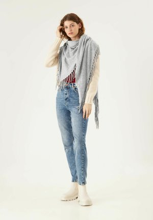 Graue Fransen-Schal, weiche Textur, über einem roten Hemd getragen, kombiniert mit hellblauen Jeans und cremefarbenen Ankle Boots. Schlichtes Design.