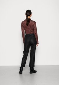 Haut à manches longues à motifs rouge et noir, associé à un pantalon noir taille haute. Modèle vu de dos, portant des bottines noires.