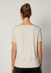 Ljusbeige kortärmad skjorta med rund halsringning och mjuk, slät textur. Sömlös design med rak fåll bak.