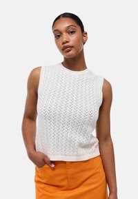 Haut en tricot blanc sans manches avec un motif texturé et un col côtelé. Associé à une jupe ajustée orange vif pour créer un contraste.