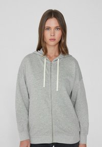 Grauer Reißverschluss-Hoodie aus weichem Stoff mit Kapuze. Verfügt über leichte Kordeln und gerippten Saum. Lockere Passform und lange Ärmel.