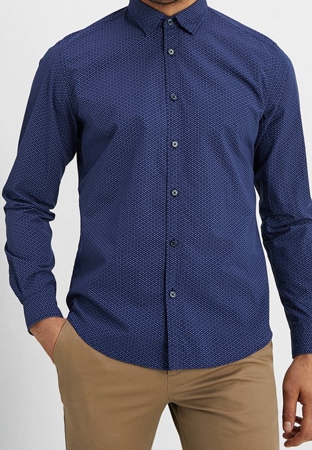 Mörkblå skjorta med knappar, prydd med ett geometriskt mönster av vita prickar, långärmad och med spetsig krage, tillverkad av mjukt tyg.
