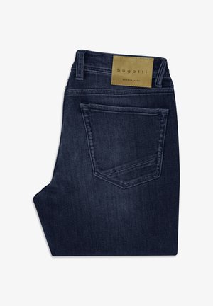 Ciemnoniebieskie podwinięte dżinsy z tylną kieszenią i jasnobrązową skórzaną metką na pasku, na której widnieje napis "bugatti handcrafted".