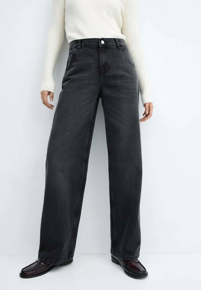 Mustat leveälahkeiset farkut, joissa korkea vyötärö, etutaskut ja napillinen kiinnitys, yhdistettynä kermaan vivahtavaan ribbineulepaitaan ja tummiin kenkiin.