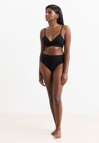 Schwarzer Bikini-Oberteil und hoch geschnittene Unterteile aus glattem Stoff. Der Oberteil hat dünne Träger und ein dreieckiges Design.