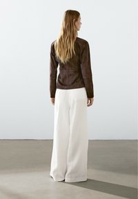 Brun mockasiner långärmad topp i kombination med lösa vita vida byxor. Outfiten har en ren design med neutrala färger och mjuka texturer.