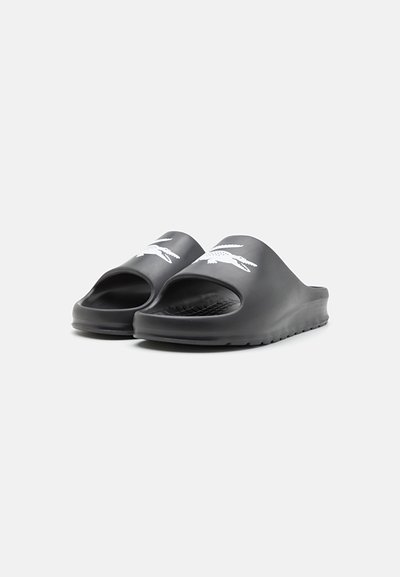 Sandales d'été noires avec une semelle texturée, design à bout ouvert et un logo blanc sur le devant. Fabriquées en matériau lisse et flexible.