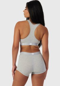 Sujeción deportiva gris con diseño de espalda nadadora, que presenta una textura suave y una banda de logo en contraste. Combinada con unas pantalones cortos hipster grises a juego.