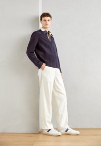 Chaqueta de cremallera azul marino con cuello blanco, pantalones anchos blancos y zapatillas blancas con detalles en azul marino. Tejido suave, corte relajado.