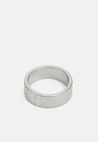 Anneau en métal argenté avec un motif gravé, intérieur lisse et arrondi, extérieur plat. Accents notables comprenant des marques de la marque.