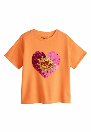 Orange kortærmet T-shirt med et stort paliet-hjerte design, der har pink, lilla og gyldne solstrålemønstre på forsiden.