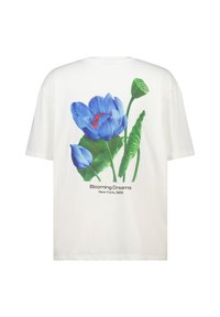 Camiseta de algodón blanca con un gran estampado de flor azul en la parte de atrás, con hojas verdes y el texto "Blooming Dreams Nueva York, 1989."