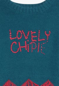 Maglione teal con testo ricamato rosso "LOVELY CHIPIE" con una finitura testurizzata e dettagli frangiati nella parte inferiore.