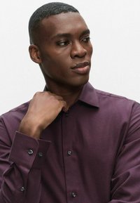 Bourgogne ternet skjorte med knapper og klassisk krave, med mørke knapper og tekstureret stof, båret af en person med kort hår.