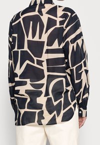 Långärmad skjorta med ett abstrakt mönster i brunt och krämfärgat, tillverkat av lättviktig tyg. Har en krage och knäppta manschetter.