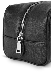 Czarna skórzana kosmetyczka o teksturowanej powierzchni, z metalowym suwakiem w kolorze srebrnym oraz małym trójkątnym elementem dekoracyjnym. Kompaktowy, prostokątny kształt.